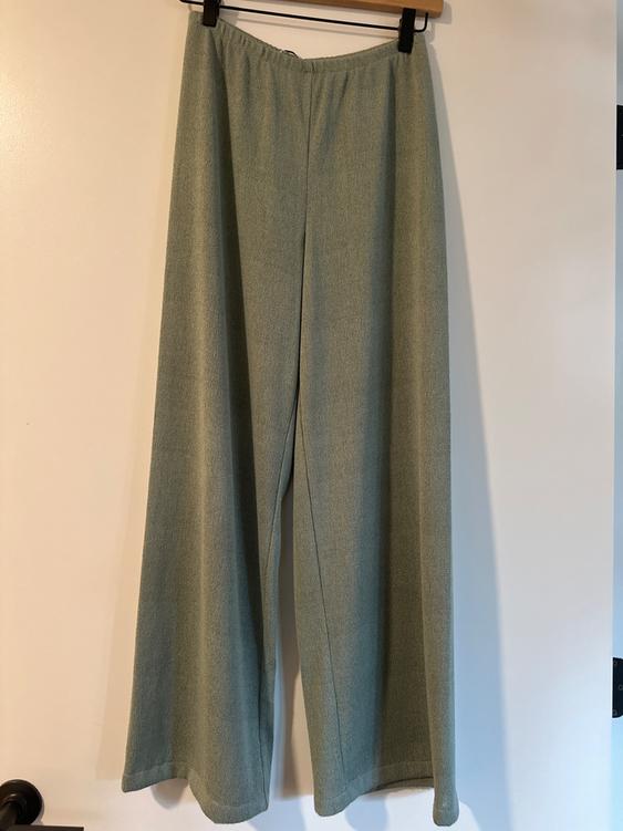 Light green wide-leg pants hanging on a hanger over a white door.