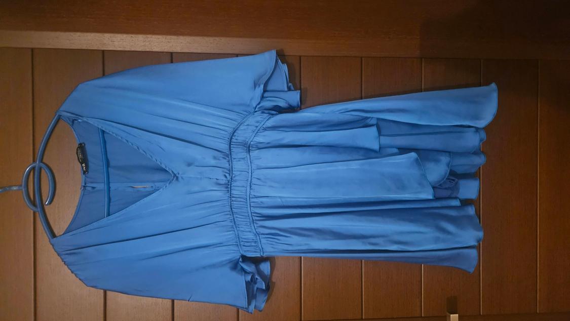 Blue dress hanging on a hanger over a wooden door. V-neck design with an elasticated waist.