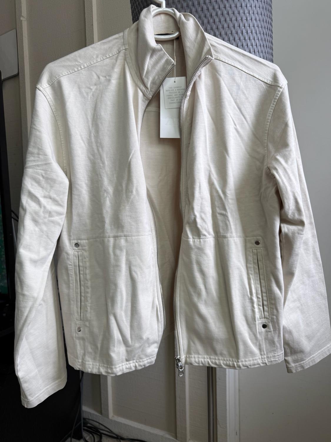 Light beige casual jacket with front zip, high collar and pockets, hanging on a white hanger indoors.