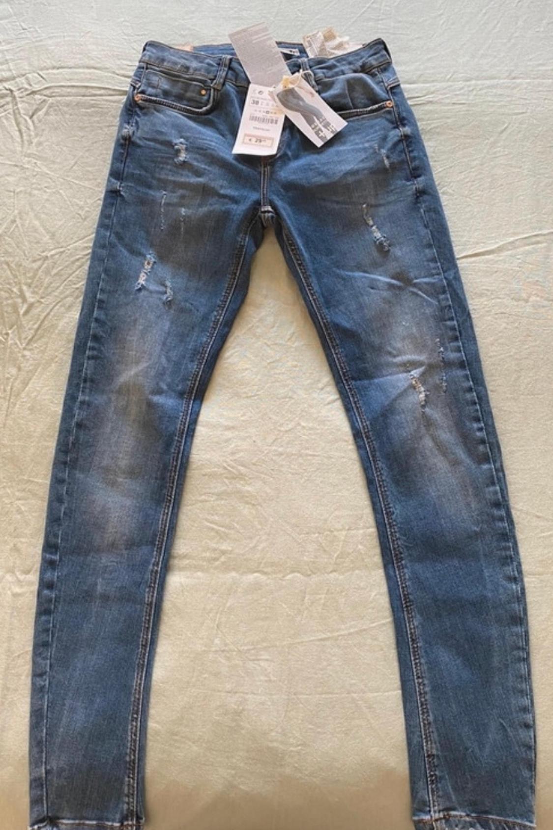 Front view of blue jeans with front pockets and distressed details.