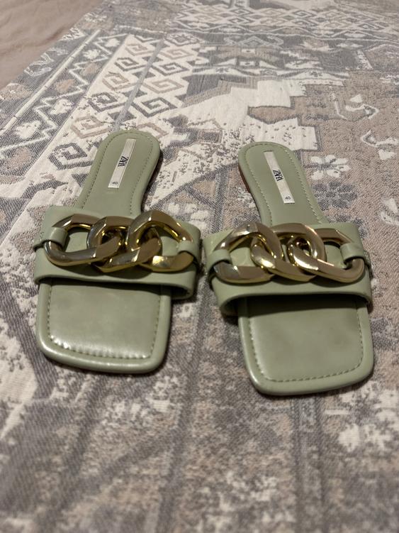 Green sandals with a gold chain on a geometric design rug. Visible tag: "ZARA 40".