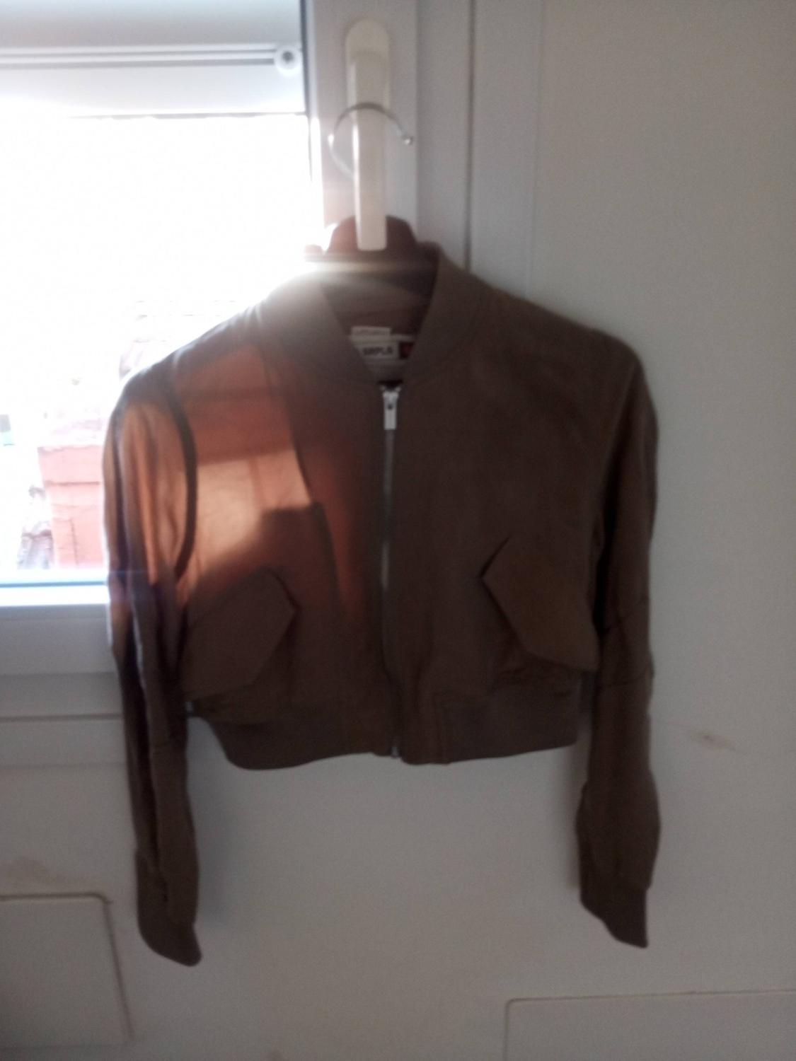 Brown jacket hanging on a white hanger in front of a window. Natural light partially illuminates the garment.