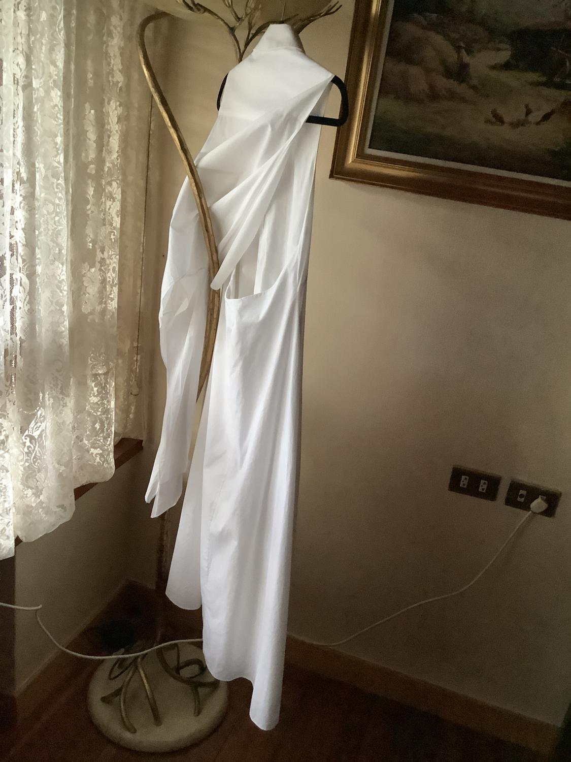 White dress hanging on a gold clothes rail next to a window with a lace curtain. Background with framed picture.