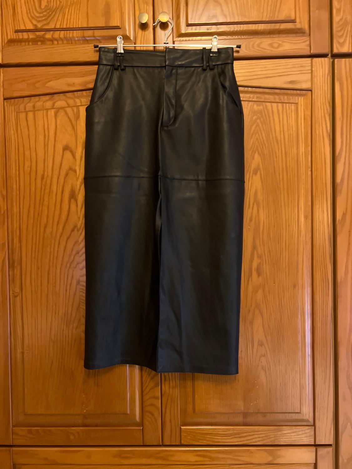 Black faux leather midi skirt with pockets and a front slit, hanging on a wooden wardrobe.