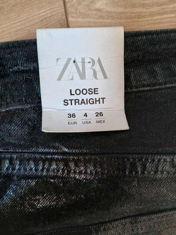 Black trousers label with text "ZARA LOOSE STRAIGHT" and sizes "36 EUR, 4 USA, 26 MEX" on a light wood background.