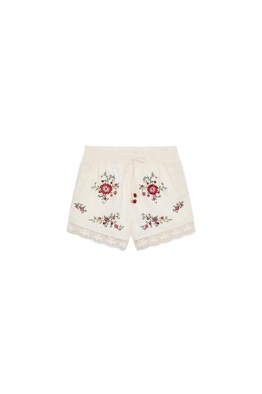 Front view of raw-cut shorts with an elasticated waist, tie, front pockets, embroidered flowers, and lace trim.