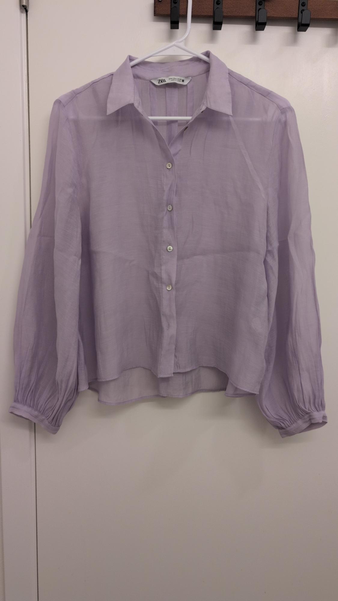 Lilac long-sleeved blouse with front buttons hanging on a white hanger against a white background. Visible label: Zara.