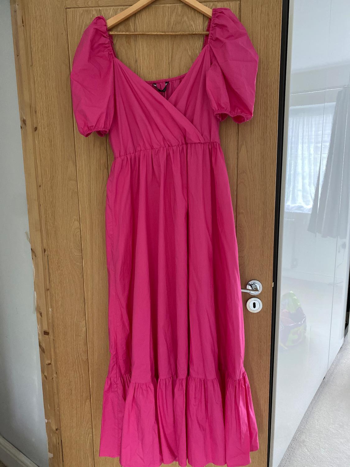 Fuchsia pink dress with puff sleeves hanging on a wooden door. Well-lit indoor setting.