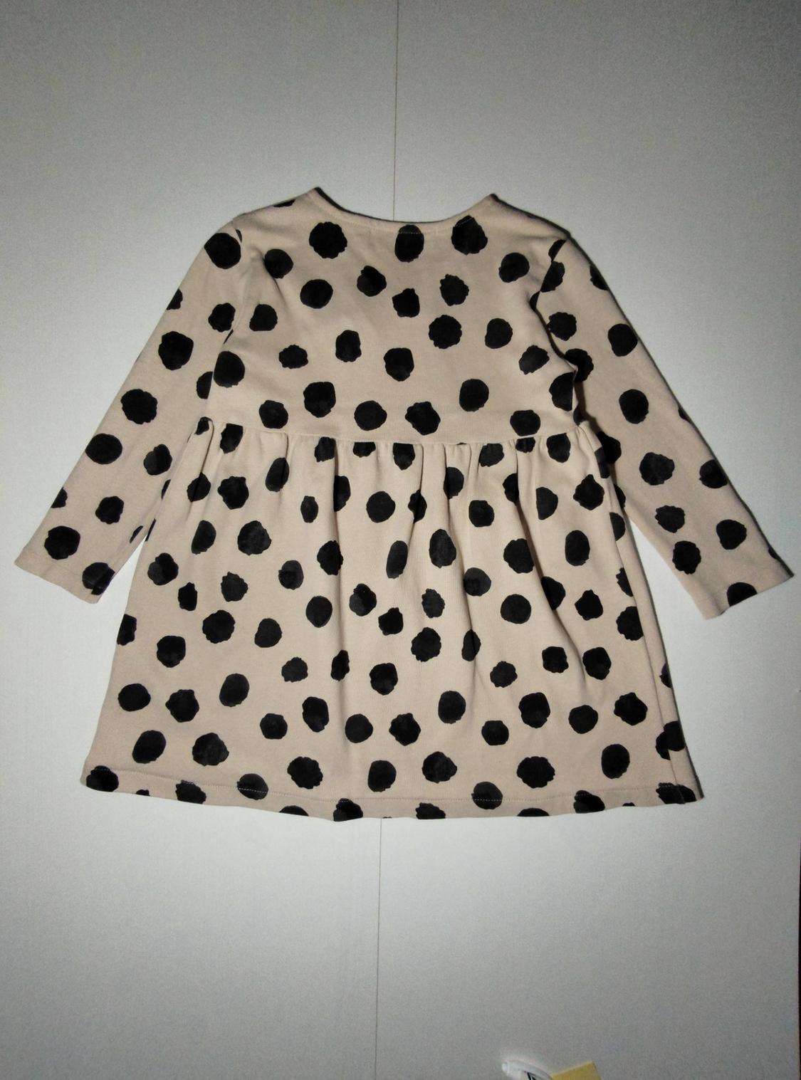 Long-sleeved beige dress with large black polka dot print, hanging on a white background.