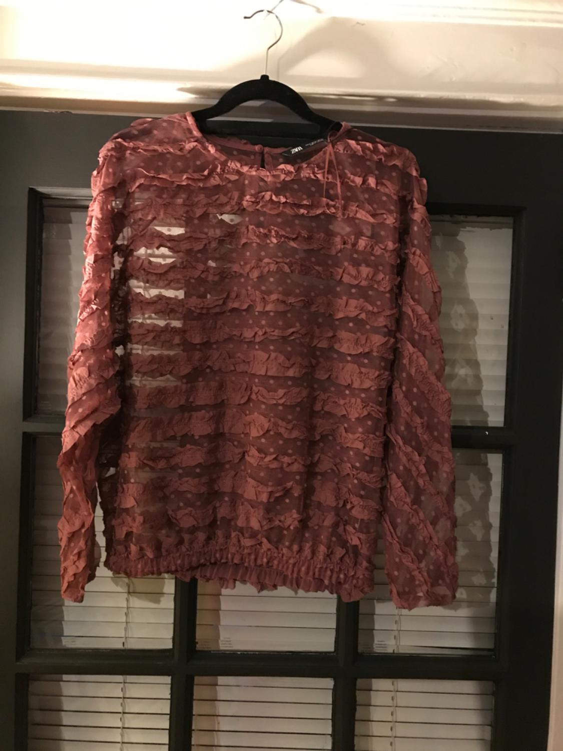 Front view of a pink blouse with frills and long sleeves.
