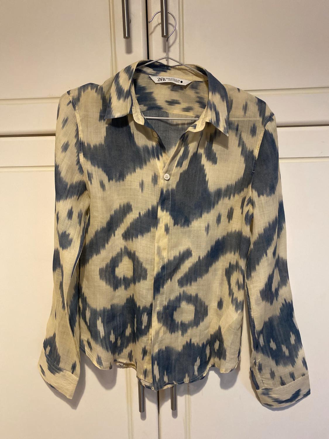 Blue and cream abstract print long-sleeved shirt hanging on a hanger in front of a white wardrobe. Label with the text ZARA.