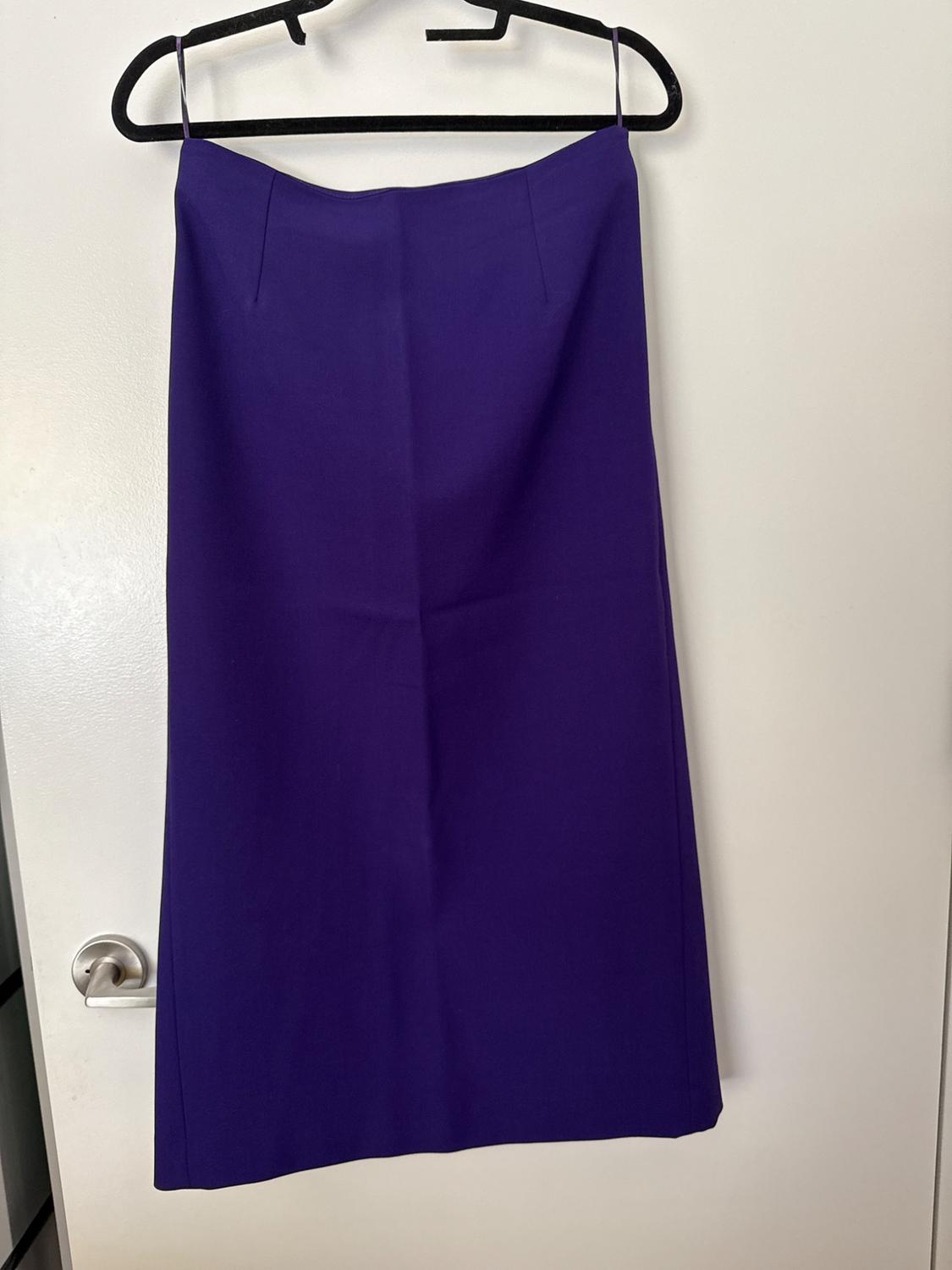 Purple straight skirt hanging on a black hanger on a white door with a metallic knob. Simple style and everyday atmosphere.