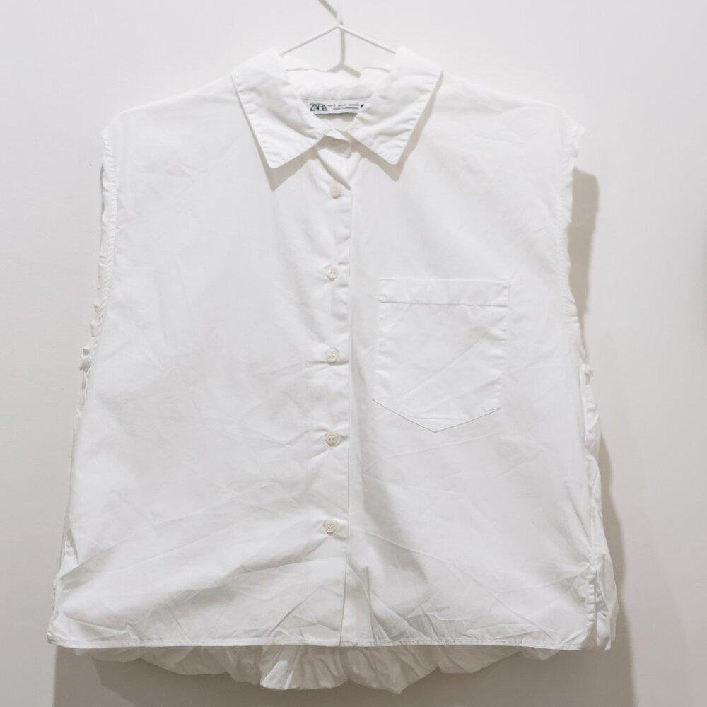 Sleeveless white Zara shirt with a classic collar, a front button placket, and a chest pocket, hanging on a hanger against a white background.