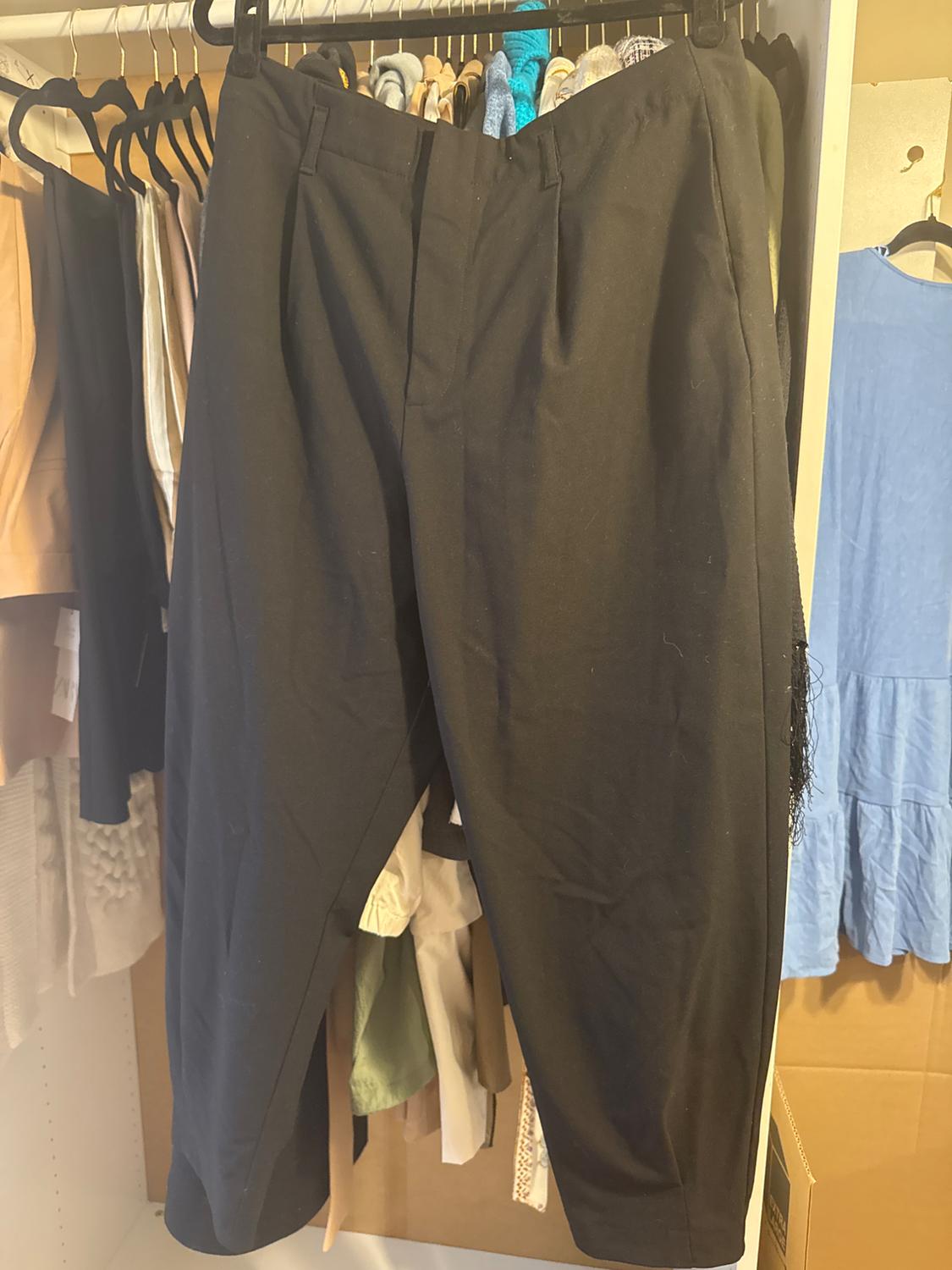 Black trousers hanging in a wardrobe, surrounded by various garments of different colours and textures on hangers.