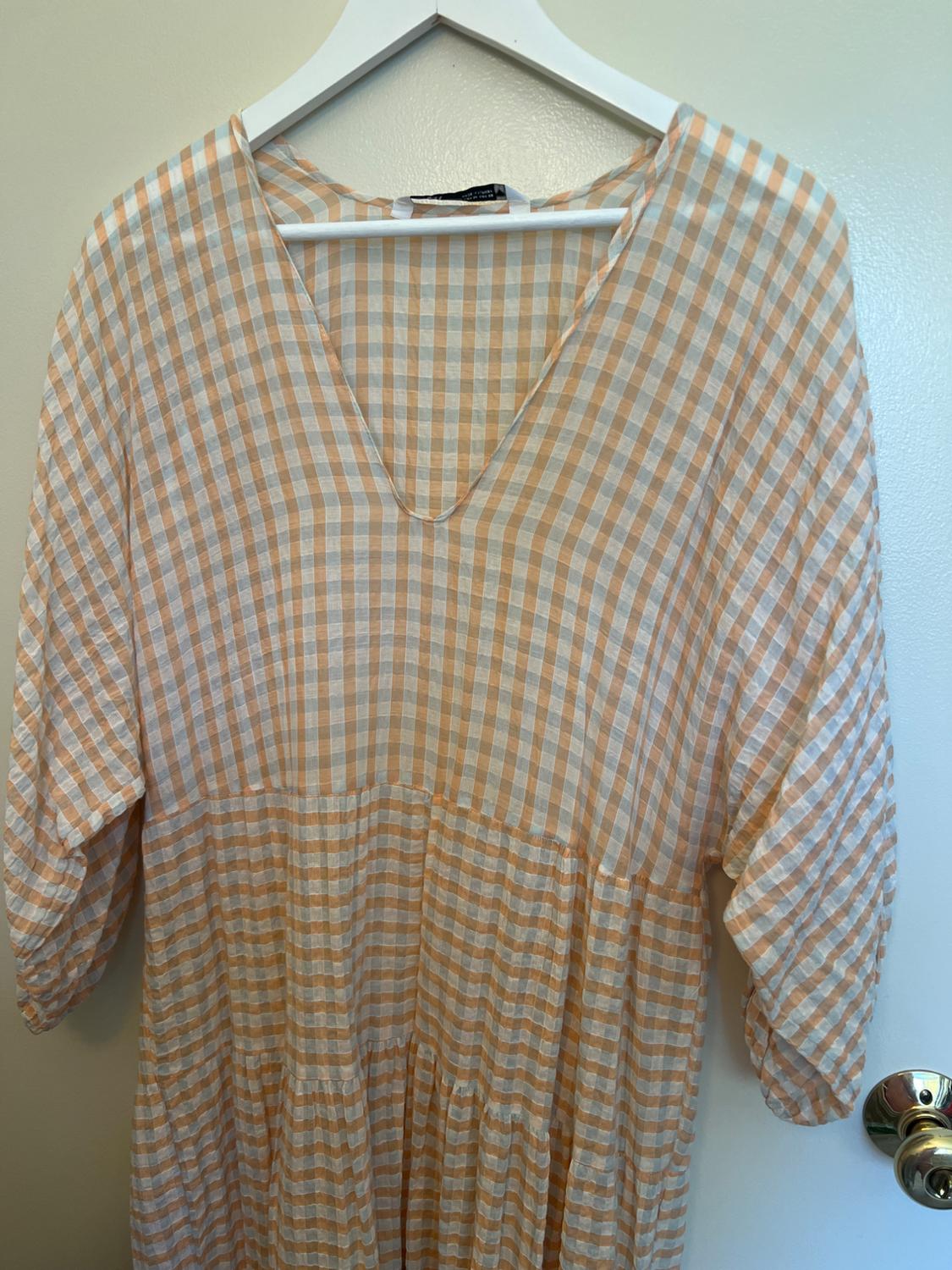 Tiered orange and white check dress with a V-neck, hanging on a white hanger on a door.