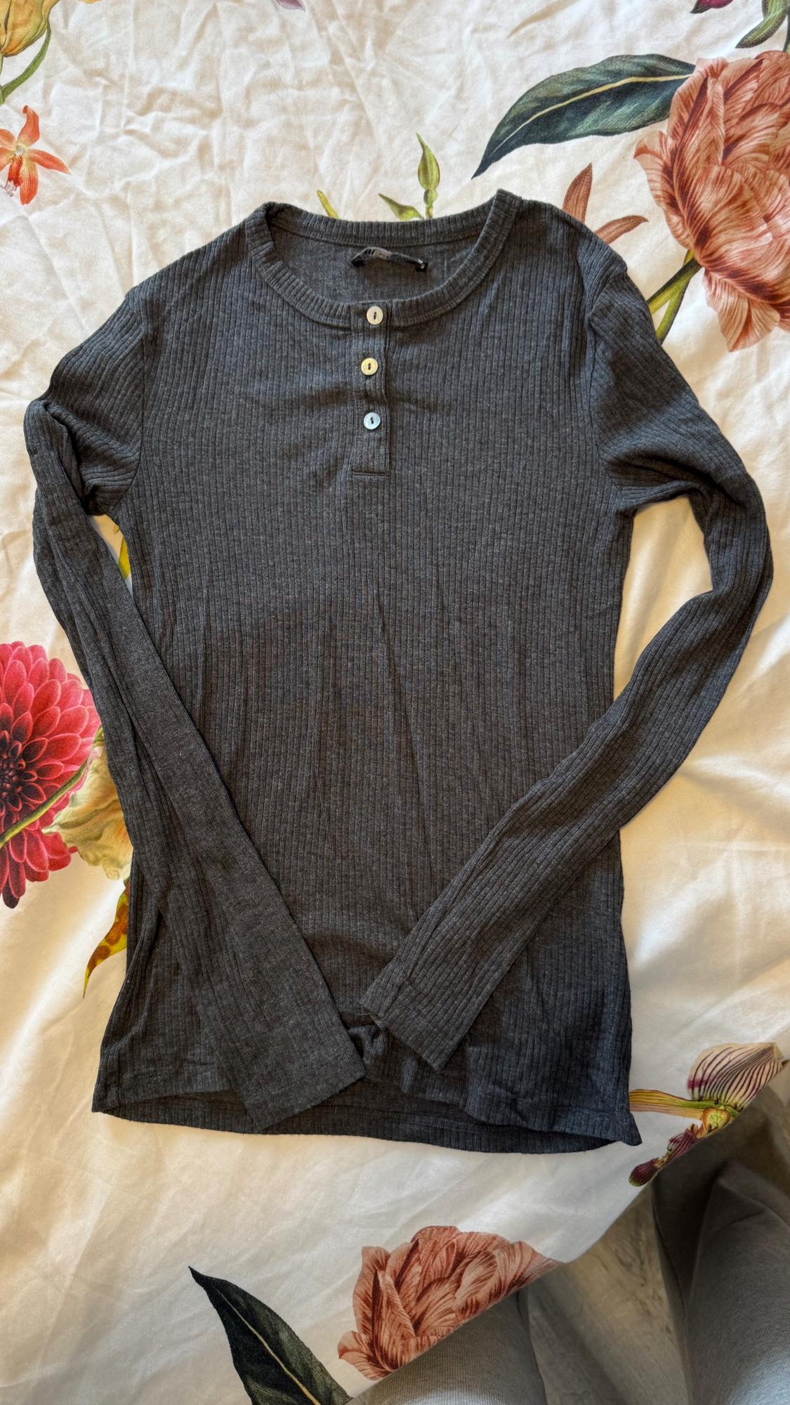 Grey long-sleeved jumper with buttons at the neck, on a white bedspread with a colourful floral print.