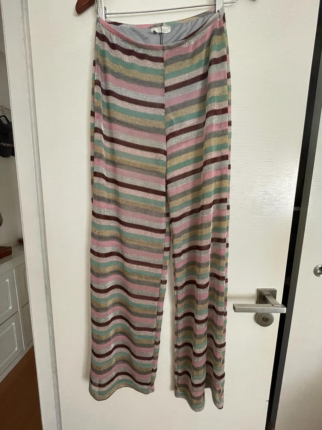 Bright pink, green, gold and maroon striped trousers hanging on a white door. In the background, a cap with the text NASA can be seen.