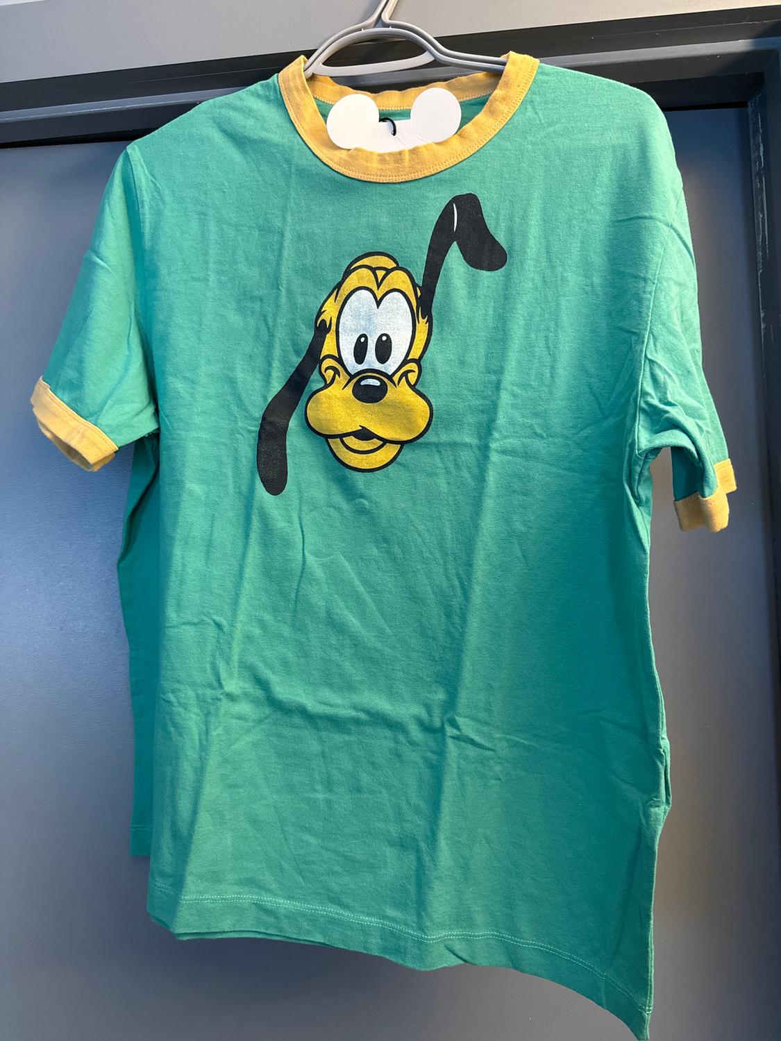 Green T-shirt with yellow collar and sleeves, featuring a cartoon character with long ears, hanging on a hanger.
