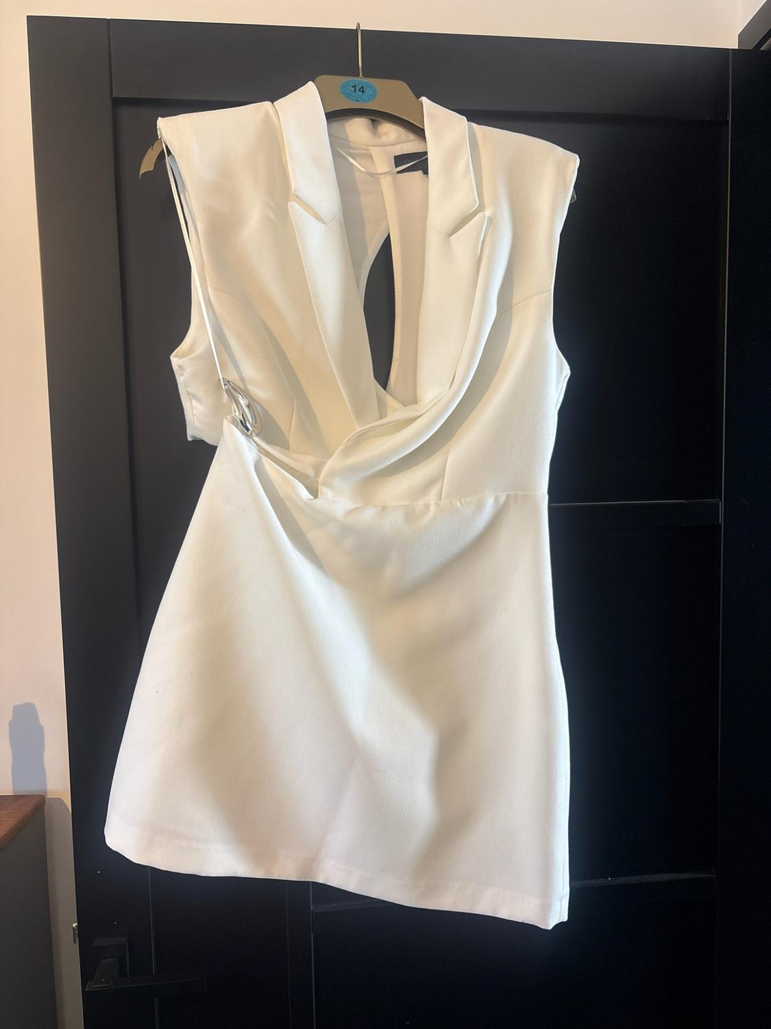 White sleeveless dress with a lapel collar, V-neck and draped detail, hanging on a black door. The hanger shows the number 14.