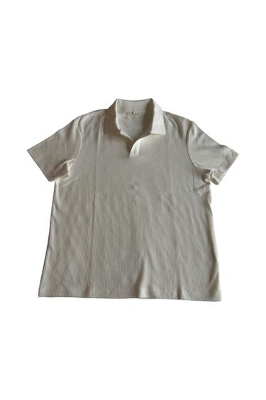 Short-sleeve ecru polo shirt with a ribbed texture. It features a classic V-slit collar without buttons on a white background.