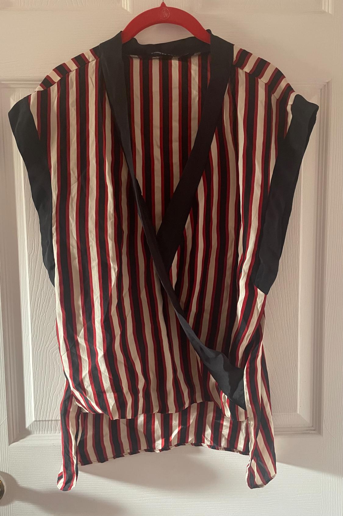 Red, black, and white vertical striped blouse hanging on a red hanger over a white door.