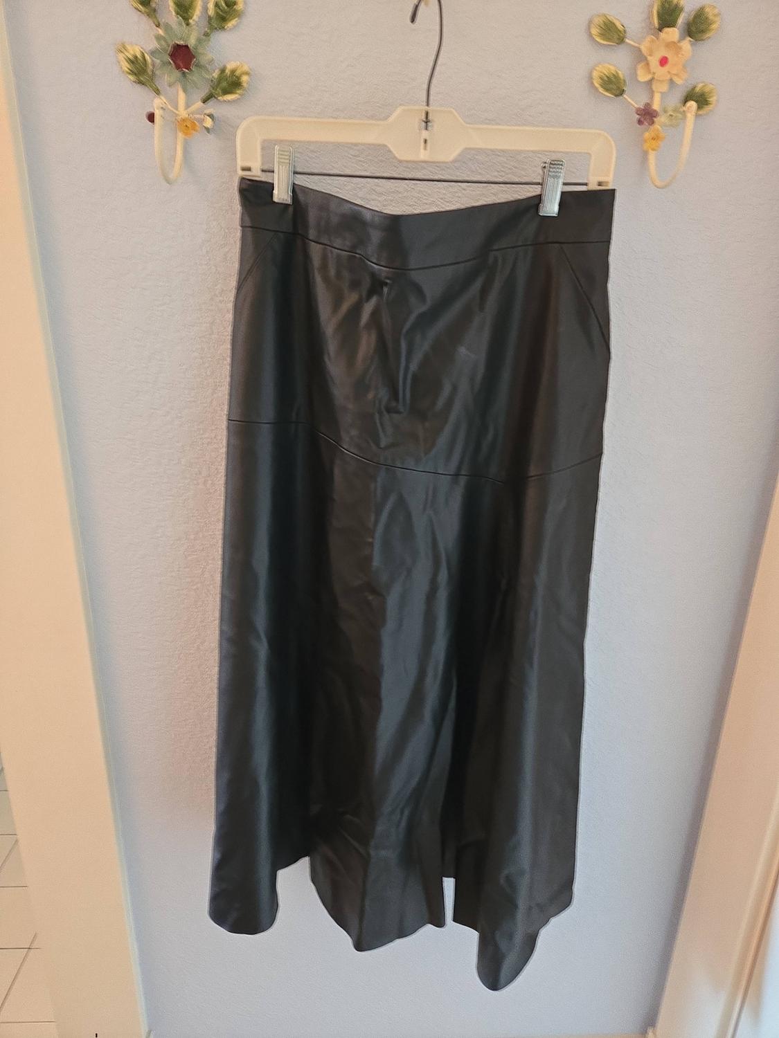 Long black faux-leather skirt hanging on a hanger against a light blue wall with two floral decorations.