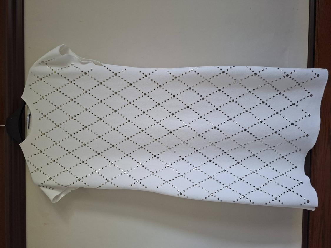White sleeveless top with a studded diamond pattern, laid out on a light-coloured surface with wooden edges.