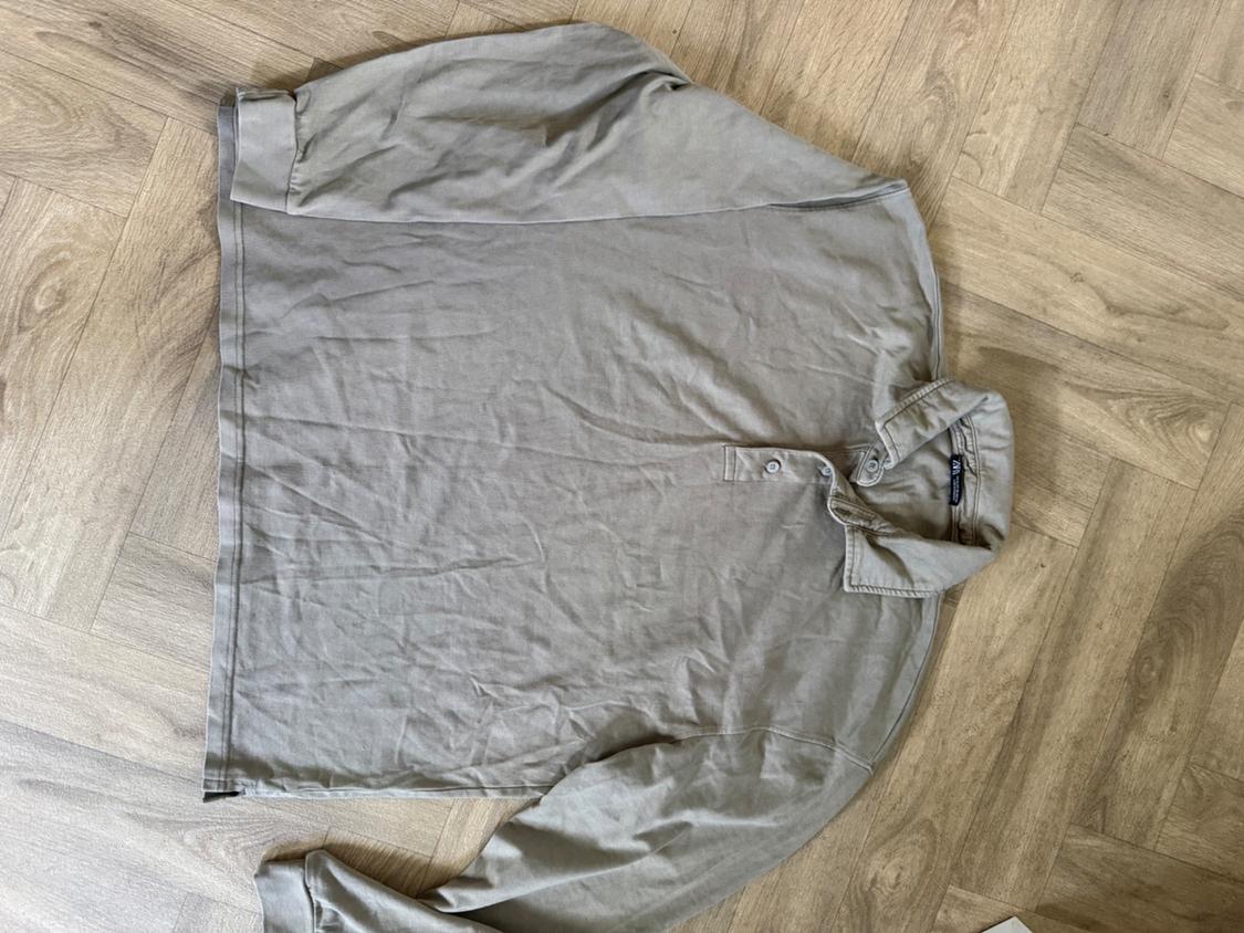 Beige long-sleeved casual polo shirt with a button-down collar, laid out on a herringbone wooden floor. ZARA interior label.