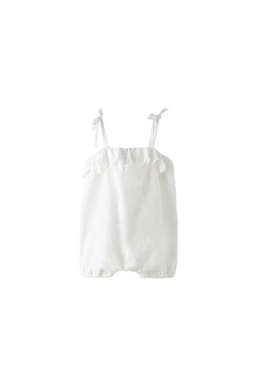White romper with tie straps, ruffle detail on the chest and subtle embroidery on a white background. Relaxed and minimalist style.