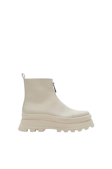 Beige platform boot with a chunky sole and side zip, on a white background. Minimalist and modern design.