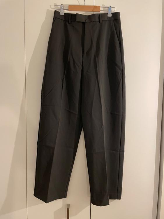 Black pants hanging on a wooden hanger against a white background. Classic design with pleats and side pockets.