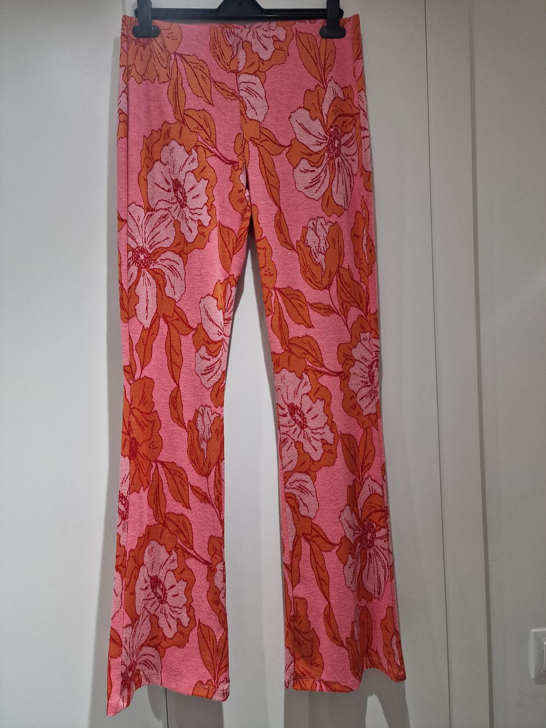 Hanging trousers with a floral print in shades of pink and orange, on a white background.