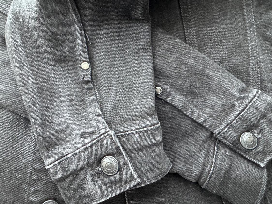 Close-up of a grey denim jacket with visible metal buttons. The texture of the fabric is clearly discernible.