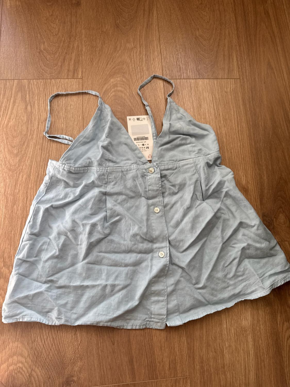 Light blue camisole blouse with a V-neck and front buttons. The labelled garment is laid flat
on a wooden floor.