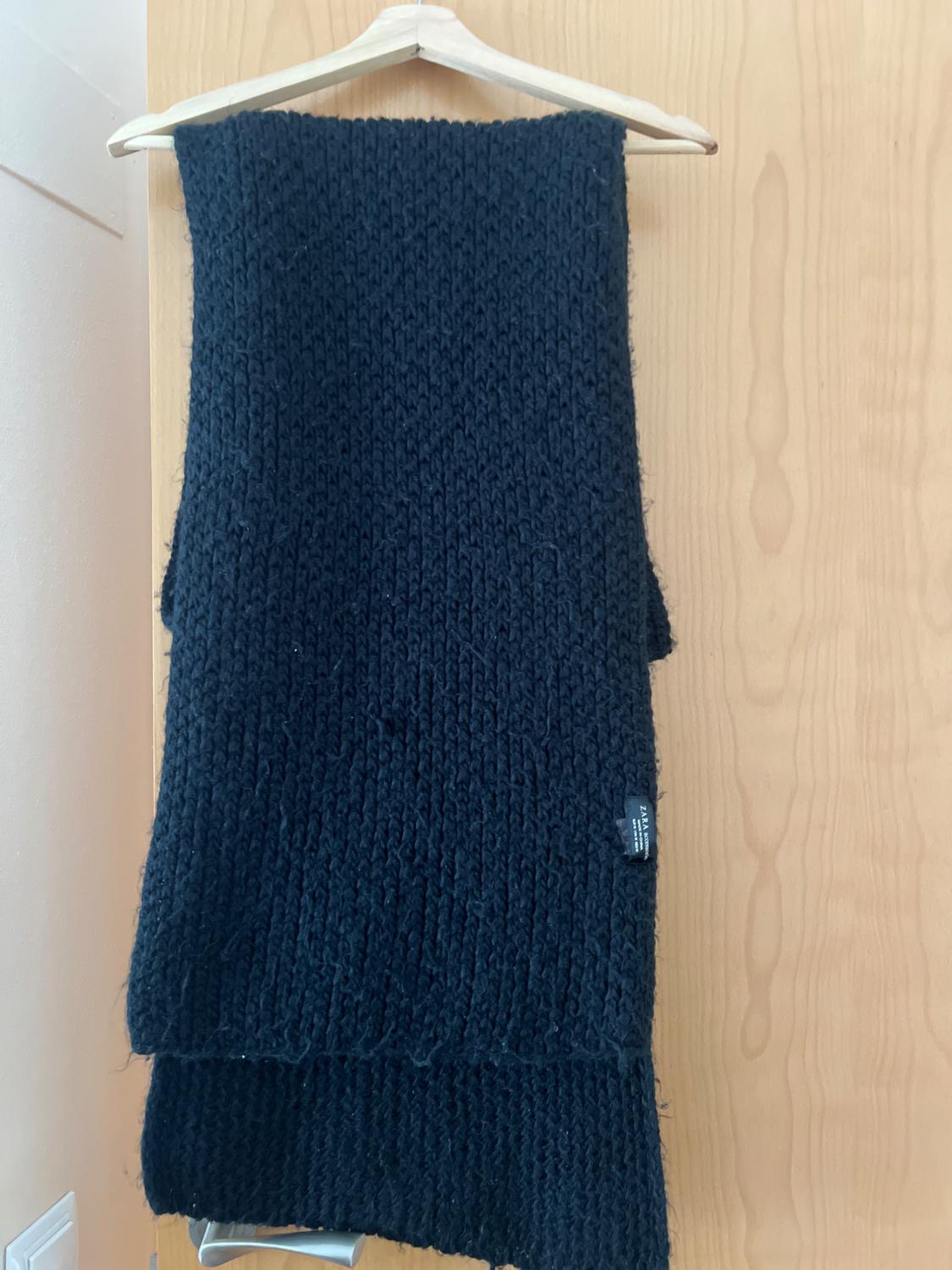 Front view of a black knitted scarf hanging on a hanger.