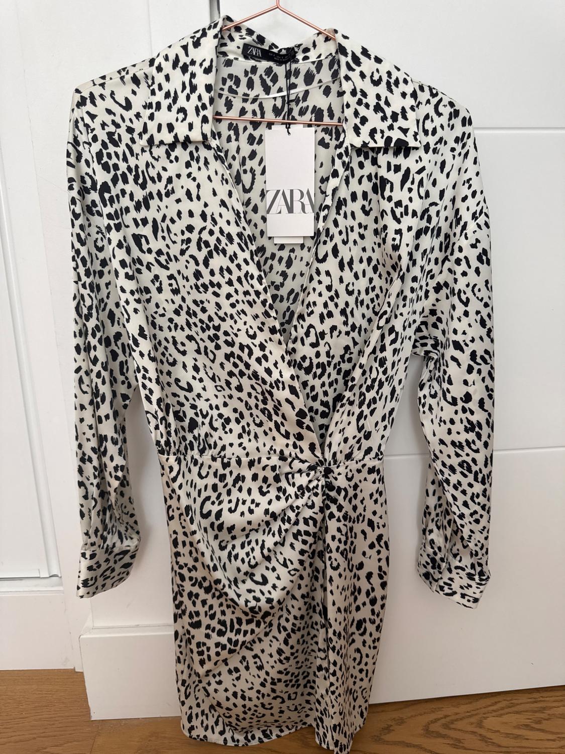 Long-sleeved dress with black spot print on a white background, hanging on a hanger. Visible label: ZARA.
