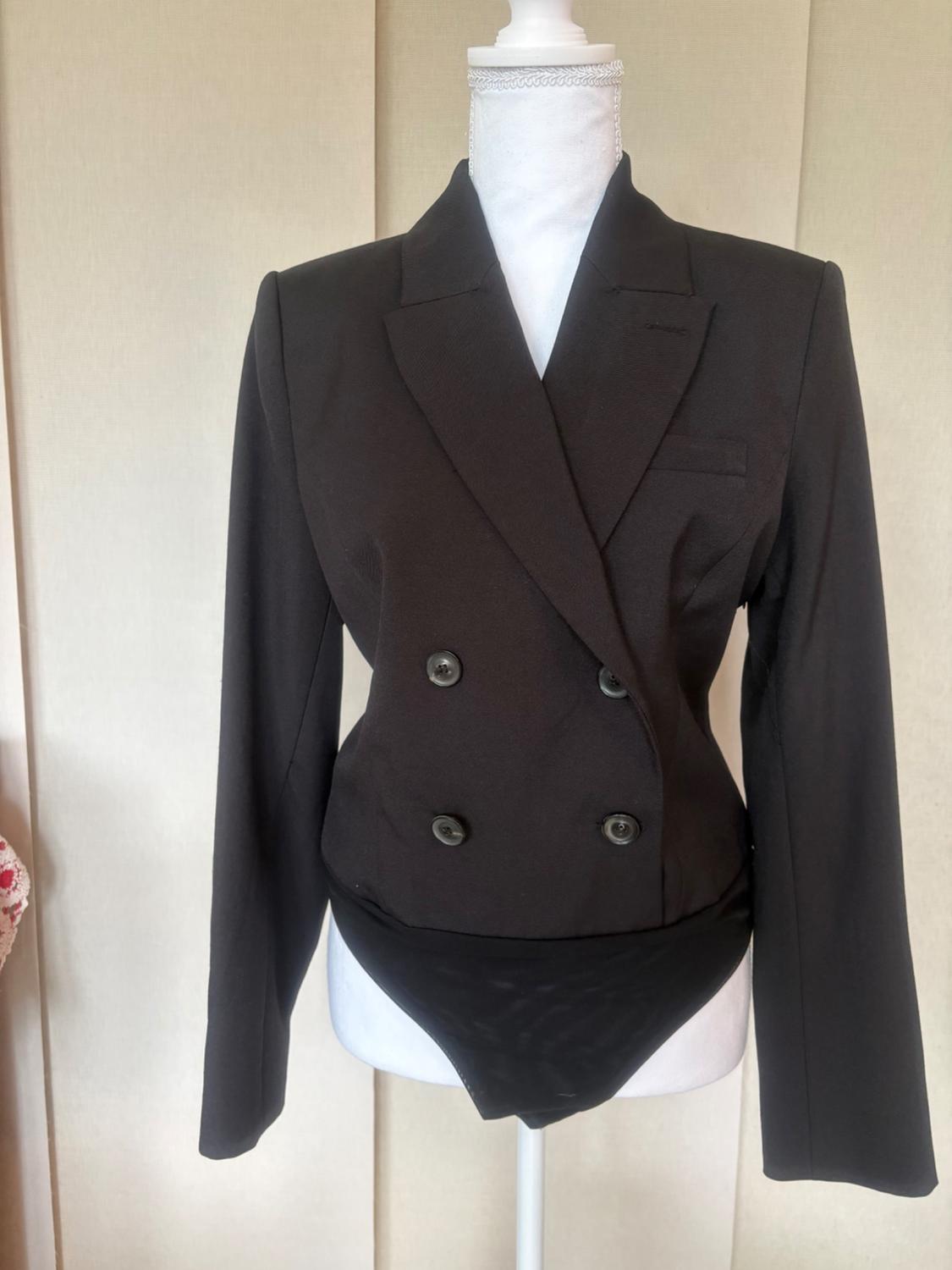 Mannequin wearing a double-breasted long-sleeve black blazer bodysuit with peak lapels against a light background.