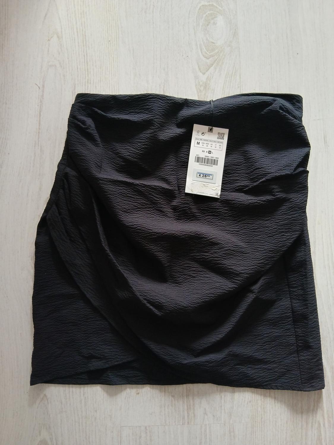 Black skirt with crinkled texture on a light floor. Visible tag with price of €26.95.
