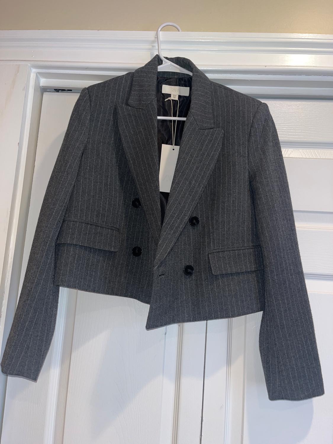 Grey jacket with vertical stripes hanging on a white hanger over a white door. Label visible inside.
