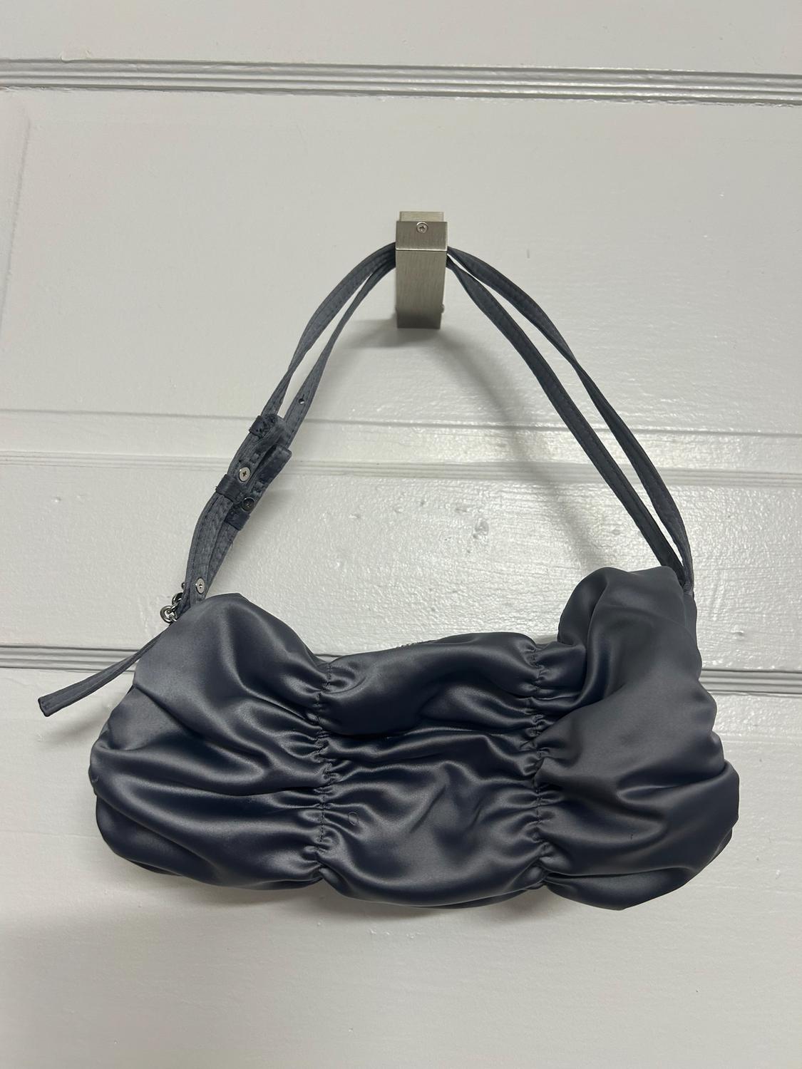Black handbag with ruched texture hanging from a hook on a white wall. Adjustable strap and elegant design.