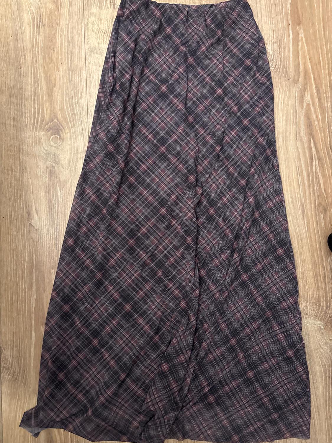 Long skirt made of checked fabric in dark tones on a light wooden floor.