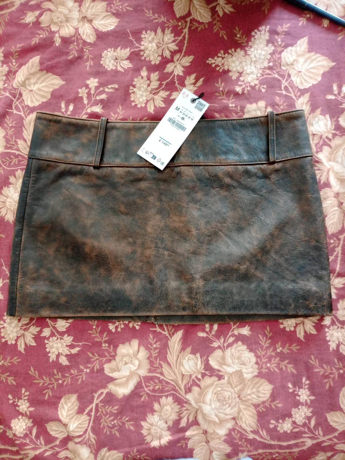 Short brown skirt with a distressed effect over red fabric with a floral print. Label with text: M M 28 M M M, €149.