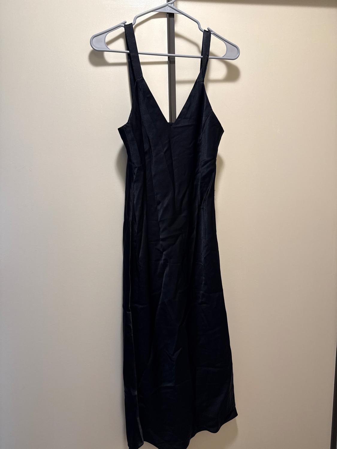 Black spaghetti strap dress with a V-neck hanging on a hanger on a light-colored door.