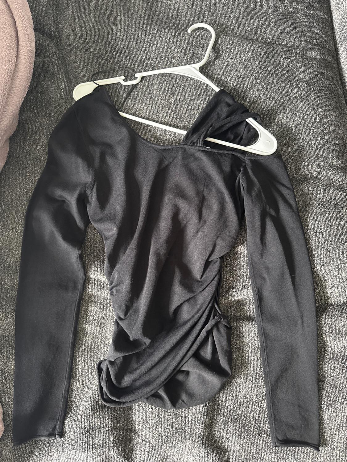 Long-sleeved black blouse with draped design, hanging on a white hanger over a gray sofa.