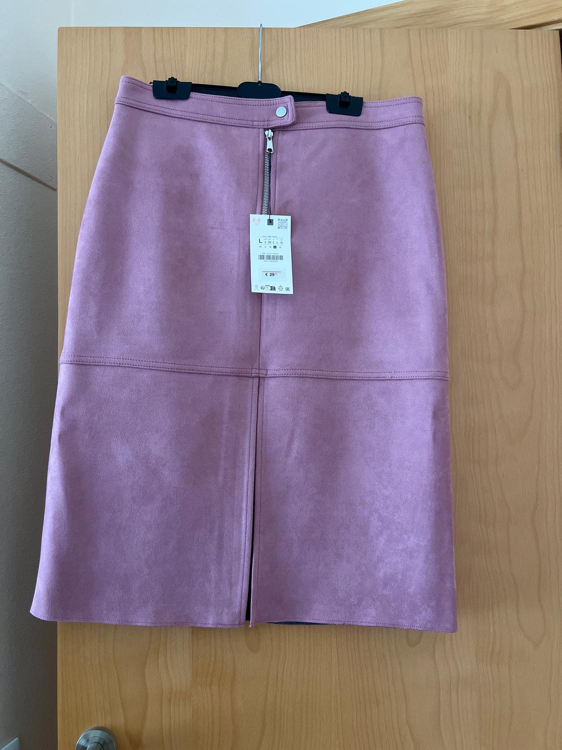 Pink skirt hanging on a wooden door, with a visible zip and price tag of 29.95 euros.
