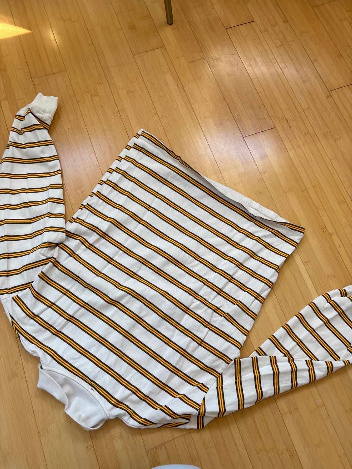 White and yellow striped sweater on a light wooden floor, with extended sleeves and natural light.