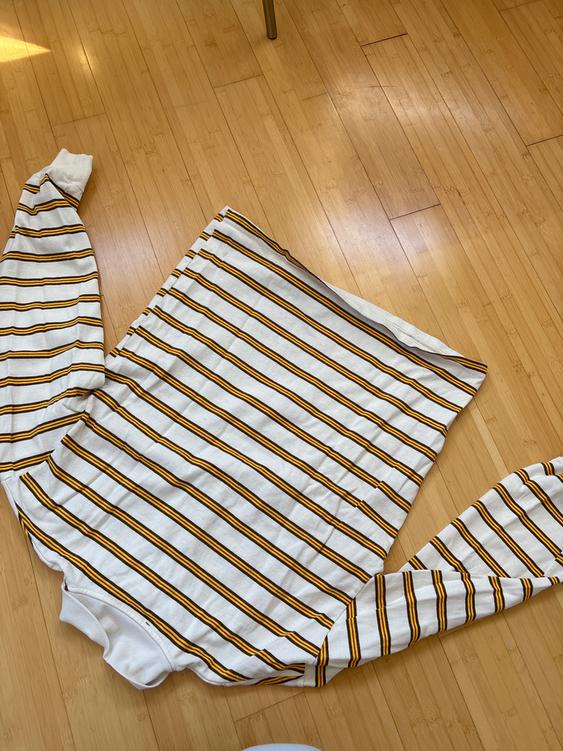 White and yellow striped sweater on a light wooden floor, with extended sleeves and natural light.