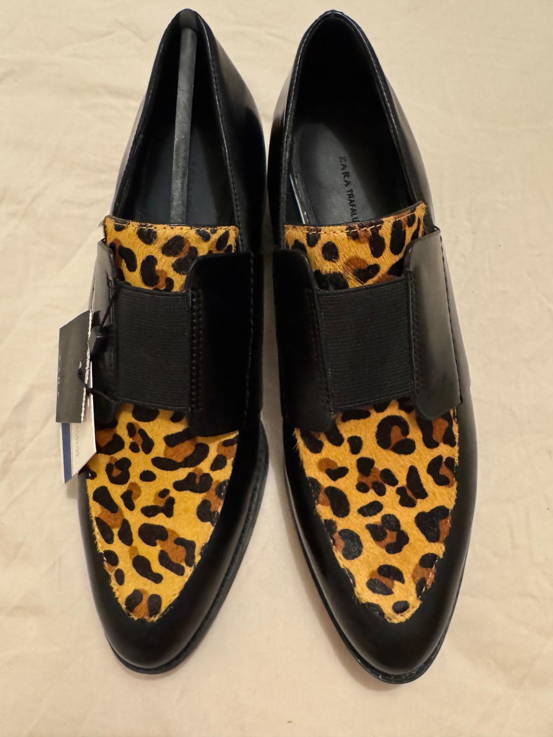 Μαύρα ίσια παπούτσια με μπροστινό πάνελ με animal print λεοπάρ και λάστιχο (ελαστική) ζώνη. Κρεμαστή ετικέτα και κείμενο «ZARA TRAFALUC» στο εσωτερικό.