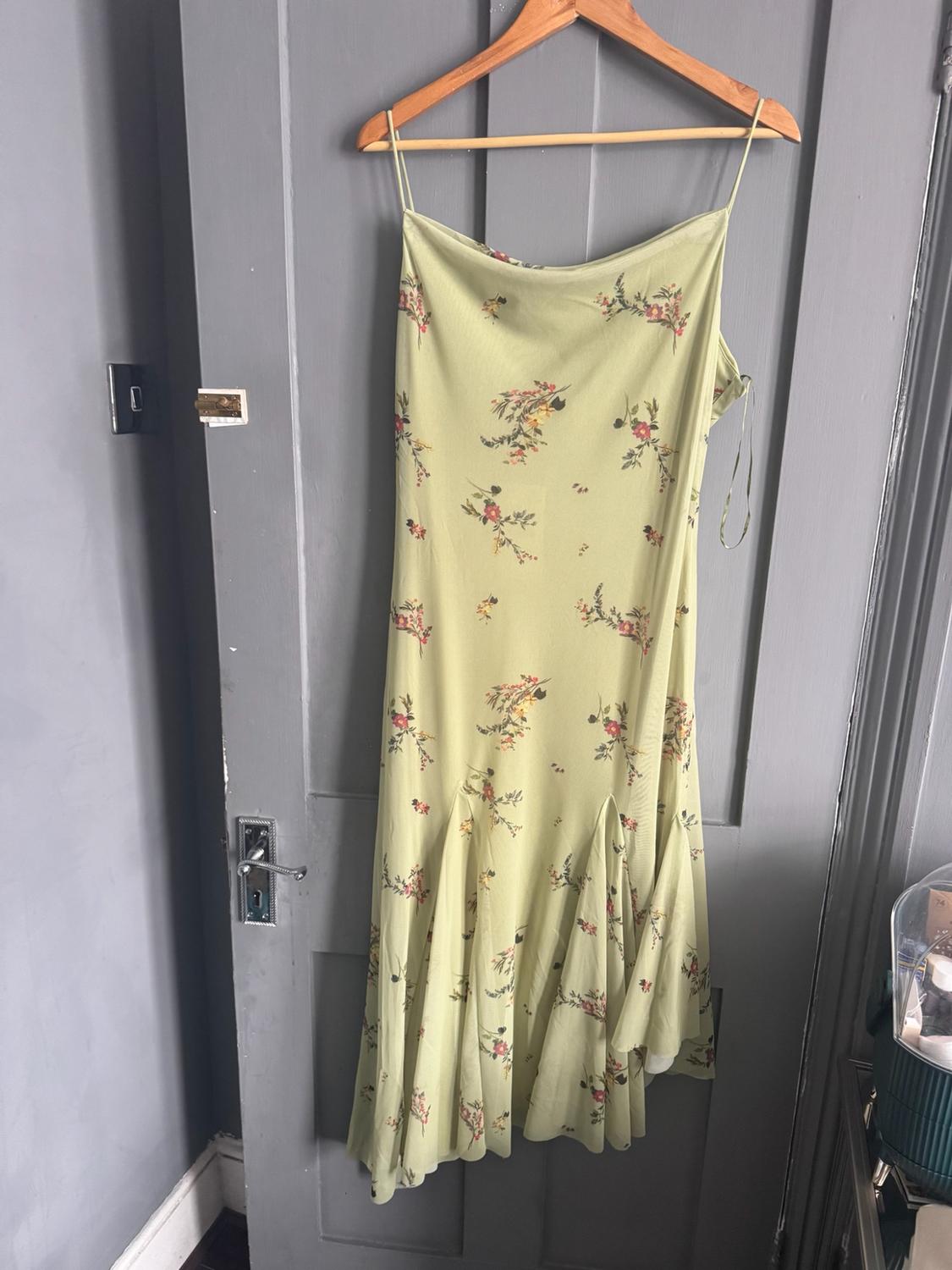 Light green strappy dress with a floral print and a flared hem, hanging on a wooden hanger over a grey door.