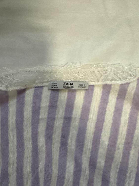 Zara clothing tag on white fabric with lace and purple and white vertical stripes. Text: "ZARA COLLECTION WOMAN".